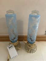 Pair of tall blue glass lamps with embossed floral design and clear textured round bases, cords coiled at base, photographed from front.