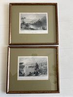 Two framed black and white landscape prints stacked and shown from above on a white background, showing wood frames and matting around prints.