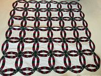 Full front view of the quilt showing the double wedding ring pattern with patchwork fabric in red, green, floral, and cream colors against a white background, laid flat on floor.