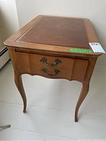 Side view of the wood side table showing curved legs and drawer with ornate handles.