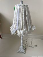 Full view of the vintage style table lamp with lace and ribbon decorated lampshade and carved white base.