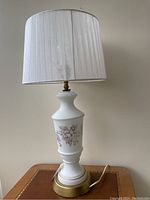 Front view of the milk glass lamp with sheer white pleated shade and visible gold floral pattern.