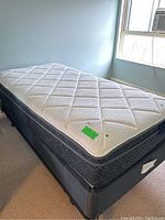 Twin pillow top mattress and box spring set with metal base on wheels shown in a furnished room.