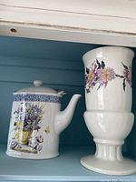 Photo showing ceramic pitcher with lid, handle, blue decorative band with floral motif.