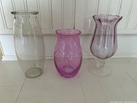 Photo showing three vases: clear tall glass, small pink vase with swirl etching, and larger stemmed pink vase with flared scalloped rim.