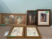 Wide shot showing all five framed artworks arranged on floor against wall: two vertically oriented Paul Peel prints with cherubic drawings to sides, various frame styles and sizes.