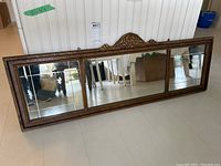 Full view of the rectangular triade mirror showing the three mirrored panels and wood frame with carved crest.