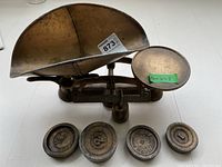 Front angled view of vintage balance scale with weighing pan and four cast iron weights in front.