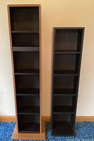 Photo of two narrow laminate shelves, one black and one brown and black, showing full front view with adjustable shelves.