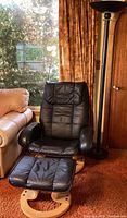 Full view of black faux leather armchair, matching ottoman and adjacent floor lamp