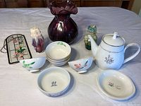 Photo of the entire lot showing large purple vase, white Noritake teapot, six small bowls, multiple candles, and a glass hanging decoration.