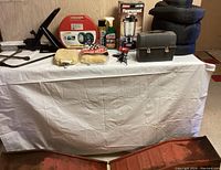 Front view of all items displayed on a white table with beige wall background, showing car repair tools and camping gear.