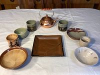 Overview image showing all pottery dishes and copper tea kettle arranged on white cloth.