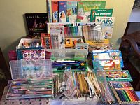 Full view of art and school supplies on table showing books, crayons, colored pencils, markers, and pens.