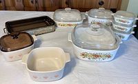 Wide view of vintage CorningWare dishes with lids, Pyrex baking pan with metal stand, and smaller dishes with plastic lids.
