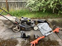 Overview of Craftsman mower, grass catcher and Black & Decker trimmer on concrete surface