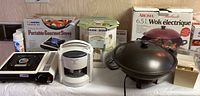 Wide view showing Aroma electric wok with lid, Black & Decker jar opener, and Iwatani portable butane stove with boxes.