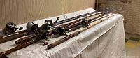 Seven fishing poles of varying lengths laid on a covered table, showing reels at the top ends.