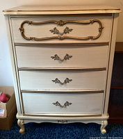 Front view of French Provincial mid-century dresser showing four drawers with ornate gold decorative trim and handles, light cream finish.