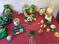 Wide view showing full assortment of frog plush toys, bunny clock, small figurines and mugs on a pink surface
