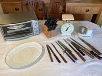 Overall view of toaster oven, scale, chopper, cutlery knives, and platter plate on a table