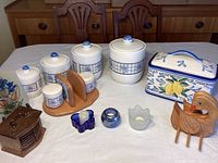 Four white ceramic canisters with blue pattern, wooden duck, ceramic bread box, small candle holders, ceramic pitcher.