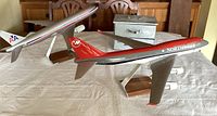 Two commercial model airplanes on wooden stands with a metal storage box behind them on a table.
