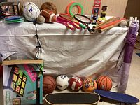 Photo showing assortment of sports balls, bats, badminton rackets, skateboards, frisbees, boxed game, and bobblehead.