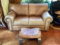 Front view of the tea-stained tan leather loveseat with the camel saddle footstool placed in front, showing the overall size and color.