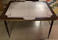 Full front view of vintage formica dining table with distinctive white patterned center and brown border with gold trim on legs and edges.