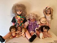 Nine vintage dolls displayed seated and standing, showing size and outfit variety