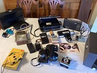 Photo showing an assortment of vintage cameras, calculators, radios and electronic devices on a table.