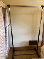 Rolling clothes rack with metal poles and black plastic feet, empty and standing upright.