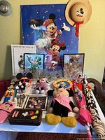 Full display of vintage Mickey and Minnie Mouse collectibles including plush dolls, framed art, glassware, slippers, and accessories.