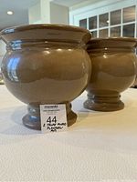 Two taupe glazed footed ceramic planters shown side by side on a table indoors.