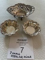 Three small sterling silver bowls displayed on a textured surface with a note card indicating '3 small sterling silver'. Two bowls are similarly shaped with scalloped edges, and a third oval bowl has pierced decoration.