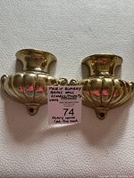 Pair of polished brass wall sconces shown from the front, close-up of design and surface.
