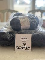 One skein of navy blue yarn wrapped in plastic, showing a MaxSold auction label with item details handwritten.