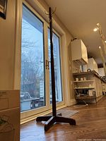 Full view of tall wooden coat stand near window showing height and structure with four legs at base.