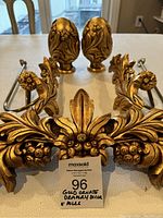 Top view of the ornate gold drapery decor pieces and poles, showing intricate leaf designs and wear on the gold finish