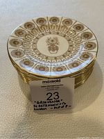 Stack of 8 cream-colored dessert plates with gold floral designs and gold rim, some visible center staining, shown from stacked side view.