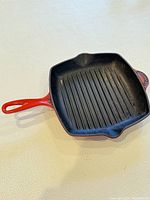 Full top view of the square grill pan showing ridged black cast iron cooking surface and red handle.