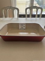 Side view of the red rectangular baking pan showing beige enamel interior and sticker with size info.