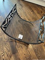 Full view photo of the metal log wood holder showing mesh bottom and decorative leaf metal sides in black finish on wood floor