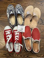 Four pairs of ladies shoes arranged on wooden floor: red Prada patent sneakers, navy and white floral slip-ons, tan Sperry thong sandals, and red slip-on flats