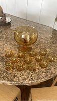 Full set of amber glass footed punch bowl, ladle, and twelve cups arranged on table