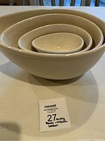 Five beige nesting bowls stacked inside each other, size increasing from smallest inside to largest outside.