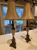 Pair of vintage table lamps on a white surface with their beige bell-shaped fabric shades and metal bases.