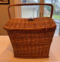Closed view of rectangular vintage wicker picnic basket with top handle and leather fastener on lid.