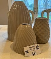 Set of three West Elm decorative vases of varying height and patterns in a beige-greige color, displayed on wood surface, photographed indoors with natural light from windows.